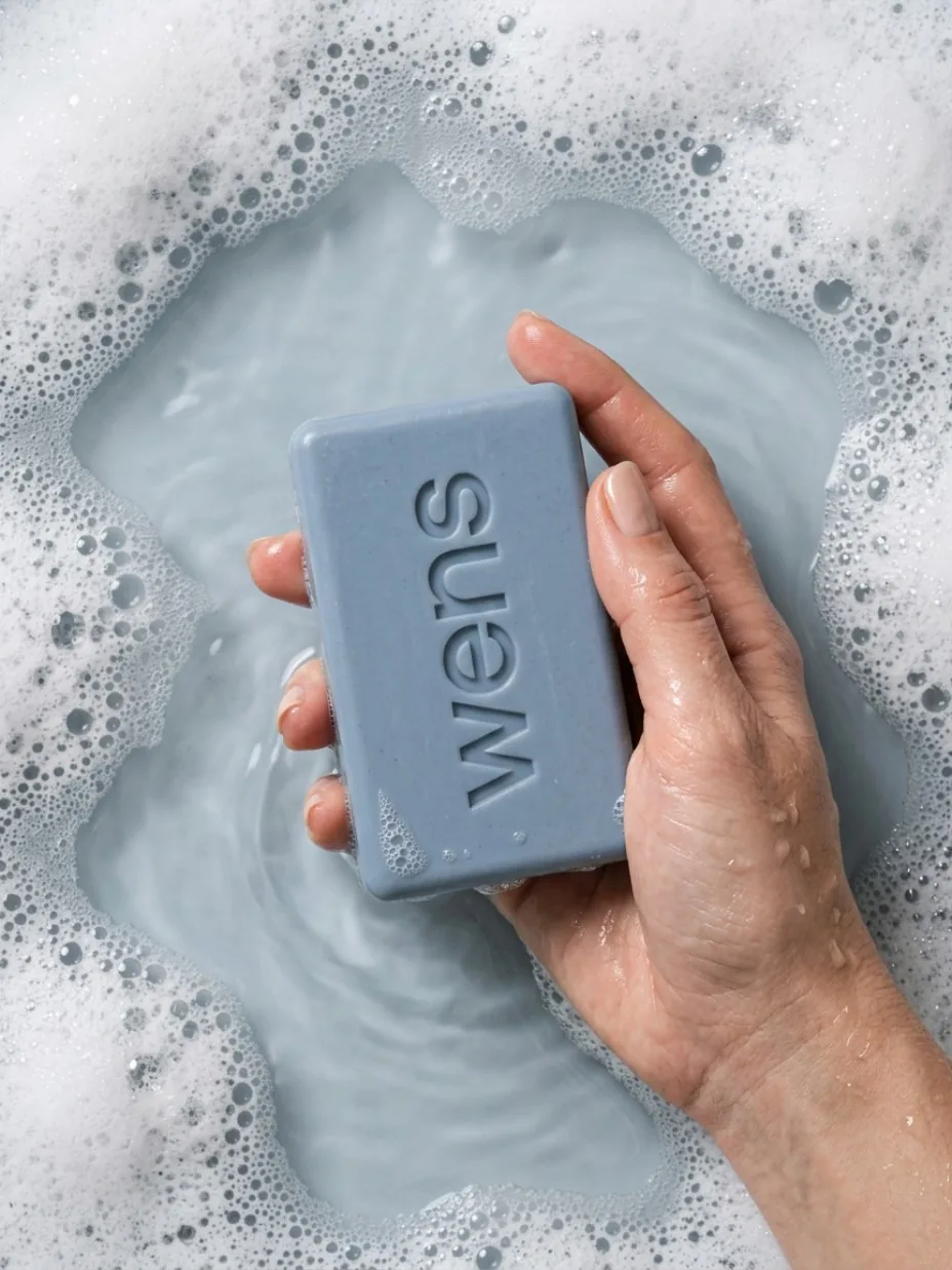 Hand holding a cleansing bar in water and foam
